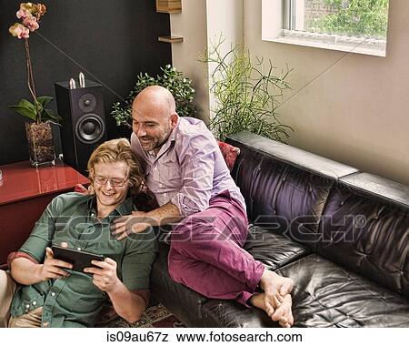 Romantic male couple reclining on sofa looking at digital tablet View Large Photo Image Stock Photo - Romantic male couple reclining on sofa looking at digital tablet. Fotosearch