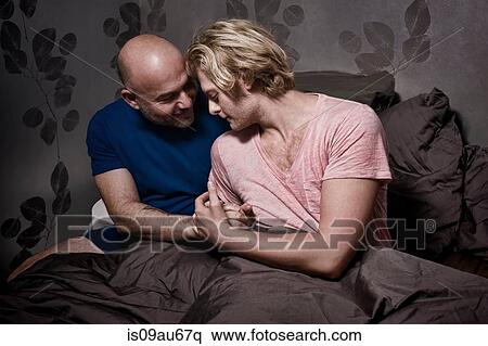 Stock Photography - Romantic male couple sitting up in bed holding hands. Fotosearch
