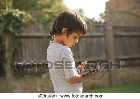 Side view of boy in garden looking down using digital tablet View Large Photo Image Stock Image - Side view of boy in garden looking down using digital tablet. Fotosearch