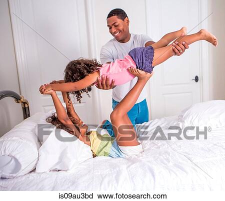 Side view of father helping daughter lying on bed to lift sister, face to face smiling View Large Photo Image Stock Image - Side view of father helping daughter lying on bed to lift sister, face to face smiling. Fotosearch