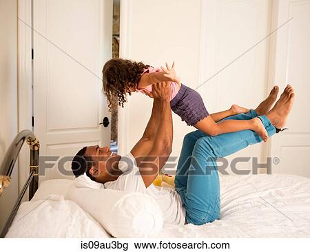 Side view of father lying on bed to lifting up daughter, face to face smiling View Large Photo Image Stock Image - Side view of father lying on bed to lifting up daughter, face to face smiling. Fotosearch