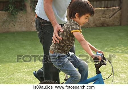 Side view of father supporting boy learning to ride bicycle View Large Photo Image Stock Photograph - Side view of father supporting boy learning to ride bicycle. Fotosearch