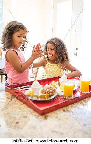 Stock Image - Sisters at home preparing breakfast, doing high five. Fotosearch