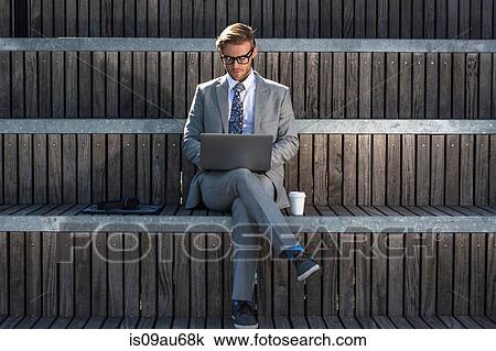Stock Image - Suited young businessman typing on laptop on city stair. Fotosearch