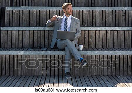 Stock Image - Suited young businessman using laptop on city stair. Fotosearch