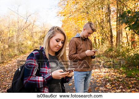 Stock Photography - Teenage boy and adult sister reading smartphone texts in autumn forest. Fotosearch