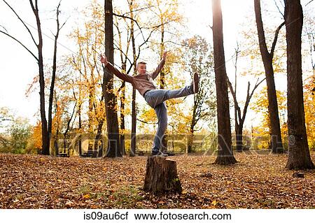 Stock Image - Teenage boy balancing on tree stump in autumn forest. Fotosearch