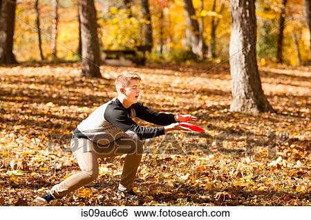 Stock Photograph - Teenage boy catching flying disc in autumn forest. Fotosearch