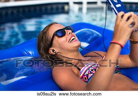 Stock Photograph - Teenager using smartphone on inflatable in swimming pool. Fotosearch