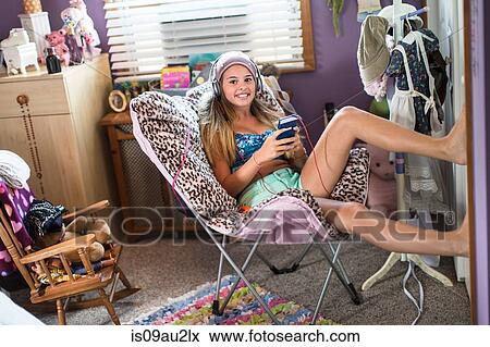 Stock Photo - Teenager using smartphone on lazy chair in bedroom. Fotosearch