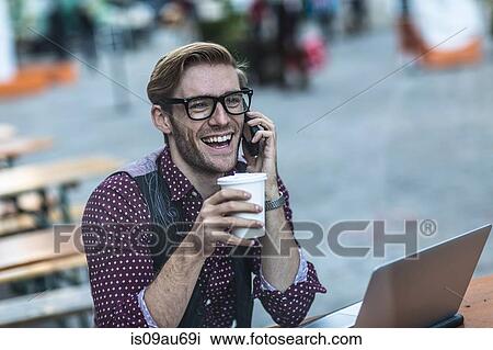 Stock Image - Young businessman chatting on smartphone at sidewalk cafe. Fotosearch
