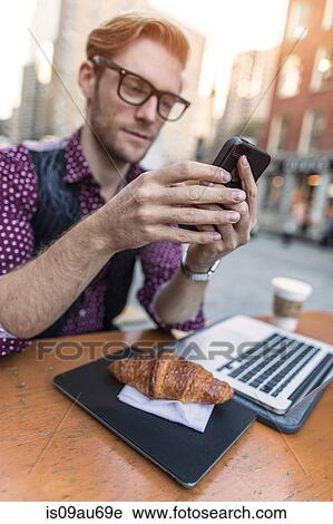 Stock Image - Young businessman having working lunch at sidewalk cafe, New York, USA. Fotosearch
