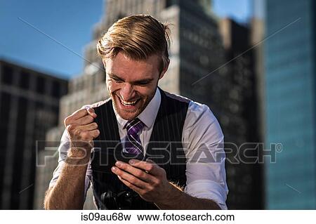 Young businessman in front of office clenching fist at smartphone, New York, USA View Large Photo Image Stock Photo - Young businessman in front of office clenching fist at smartphone, New York, USA. Fotosearch