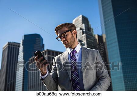 Young businessman in front of office building reading smartphone texts, New York, USA View Large Photo Image Stock Photography - Young businessman in front of office building reading smartphone texts, New York, USA. Fotosearch