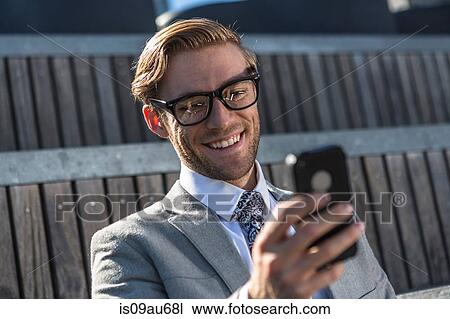 Stock Image - Young businessman reading smartphone text in city. Fotosearch