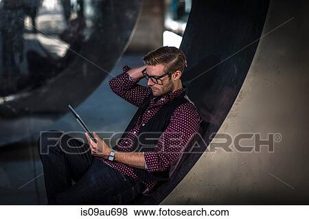 Young businessman reclining on curved wall reading digital tablet View Large Photo Image Stock Photo - Young businessman reclining on curved wall reading digital tablet. Fotosearch