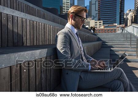 Young businessman sitting on stair typing on laptop, New York, USA View Large Photo Image Picture - Young businessman sitting on stair typing on laptop, New York, USA. Fotosearch