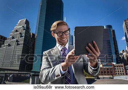 Stock Photography - Young businessman using digital tablet touchscreen in front of office, New York, USA. Fotosearch