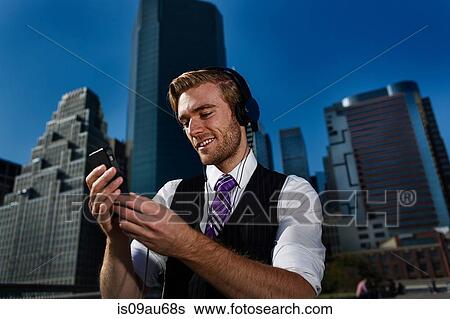 Young businessman wearing headphones reading text messages in front of office, New York, USA View Large Photo Image Stock Photograph - Young businessman wearing headphones reading text messages in front of office, New York, USA. Fotosearch