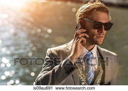 Young businessman wearing sunglasses talking on smartphone on waterfront View Large Photo Image Stock Image - Young businessman wearing sunglasses talking on smartphone on waterfront. Fotosearch