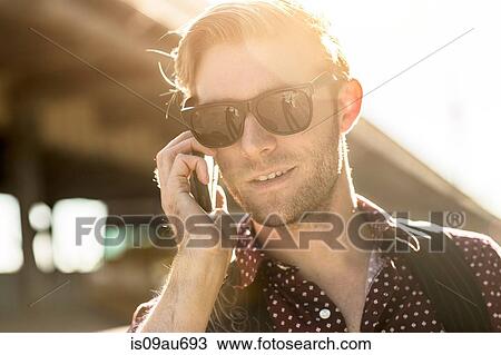 Stock Image - Young businessman wearing sunglasses talking on smartphone on city street. Fotosearch