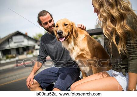 Stock Image - Young couple with dog sitting in back of jeep. Fotosearch