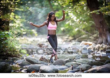 Stock Photograph - Young female hiker stepping over forest river rocks. Fotosearch