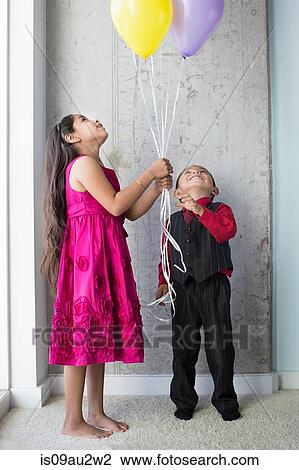 Stock Image - Young girl and boy, holding balloons. Fotosearch
