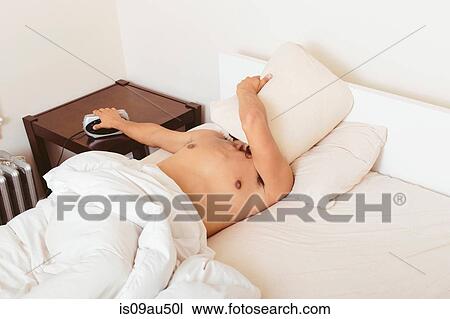 Young man in bed, covering face with pillow, turning off alarm clock View Large Photo Image Stock Image - Young man in bed, covering face with pillow, turning off alarm clock. Fotosearch