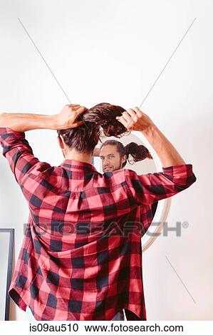 Young man looking in mirror, putting hair in ponytail, rear view View Large Photo Image Stock Image - Young man looking in mirror, putting hair in ponytail, rear view. Fotosearch