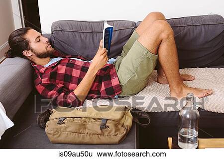 Stock Photograph - Young man relaxing on sofa, reading book. Fotosearch