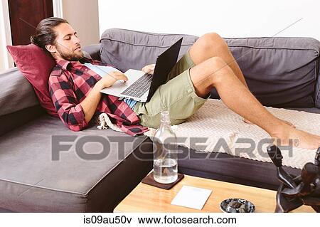 Stock Photo - Young man relaxing on sofa, using laptop. Fotosearch
