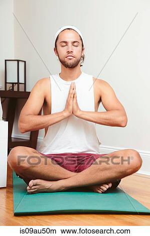 Picture - Young man sitting on yoga mat, in lotus position. Fotosearch