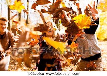 Stock Image - Young woman and two teenage brothers throwing autumn leaves in forest. Fotosearch