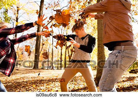 Stock Photo - Young woman and two teenage brothers throwing leaves at each other in autumn forest. Fotosearch