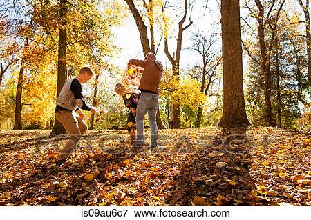 Stock Photo - Young woman playfighting with two teenage brothers in autumn forest. Fotosearch