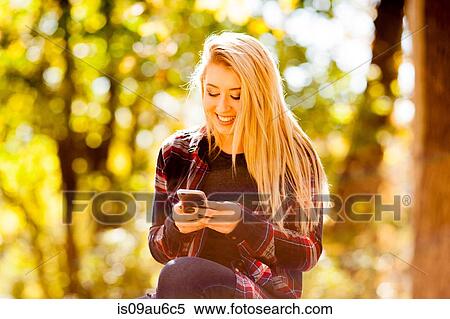 Stock Photography - Young woman reading smartphone text in autumn forest. Fotosearch