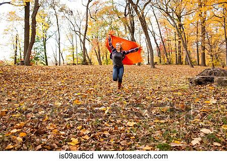 Stock Image - Young woman running and holding up blanket in autumn forest. Fotosearch