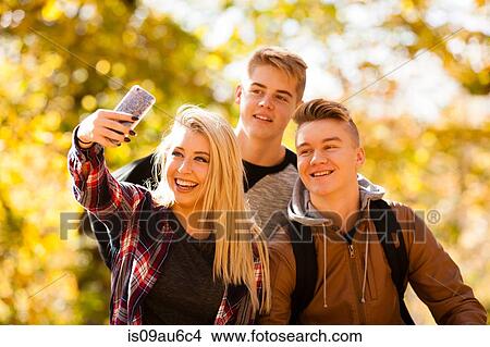 Picture - Young woman taking selfie with two teenage brothers in autumn forest. Fotosearch