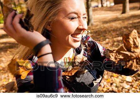 Stock Photo - Young woman throwing autumn leaves in forest. Fotosearch