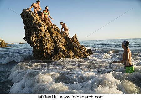 Stock Photograph - Adult friends wading and climbing on rock formation at Newport Beach, California, USA. Fotosearch
