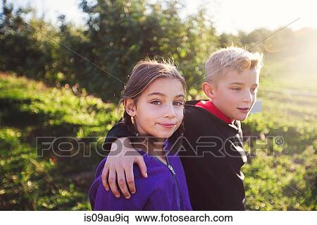 Boy in orchard with arms around girl, looking at camera smiling View Large Photo Image Stock Photography - Boy in orchard with arms around girl, looking at camera smiling. Fotosearch
