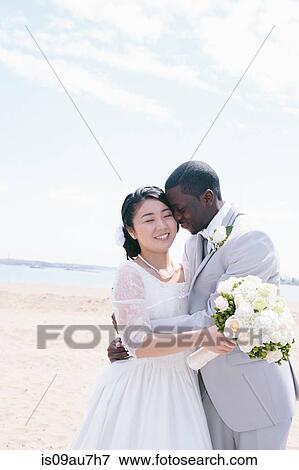 Bride and bridegroom on beach holding bridal bouquet hugging, smiling View Large Photo Image Stock Photo - Bride and bridegroom on beach holding bridal bouquet hugging, smiling. Fotosearch