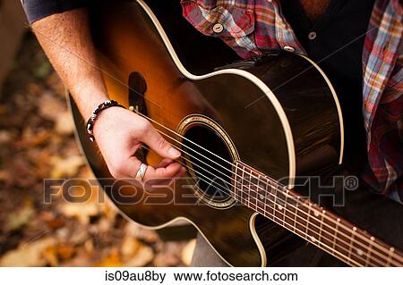 Stock Photo - Cropped shot of young man playing guitar in autumn forest. Fotosearch