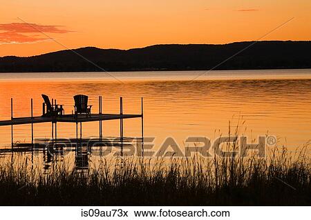 Stock Photo - Dock with chairs, on lake, at sunset in summer, Quebec, Canada. Fotosearch
