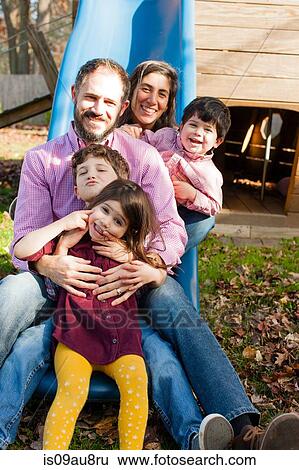 Family in a row between each others legs on playground slide, looking at camera smiling View Large Photo Image Stock Photograph - Family in a row between each others legs on playground slide, looking at camera smiling. Fotosearch