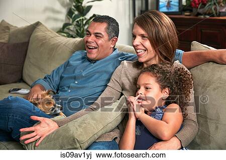 Stock Image - Family sitting together side by side on sofa looking away smiling. Fotosearch