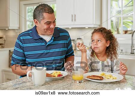 Father and daughter side by side at kitchen counter eating breakfast smiling View Large Photo Image Stock Photo - Father and daughter side by side at kitchen counter eating breakfast smiling. Fotosearch