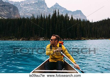 Stock Image - Front view of mid adult man paddling canoe, looking away, Moraine lake, Banff National Park, Alberta Canada. Fotosearch