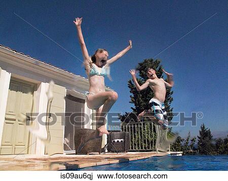 Stock Image - Girl and teenage brother jumping into apartment swimming pool. Fotosearch